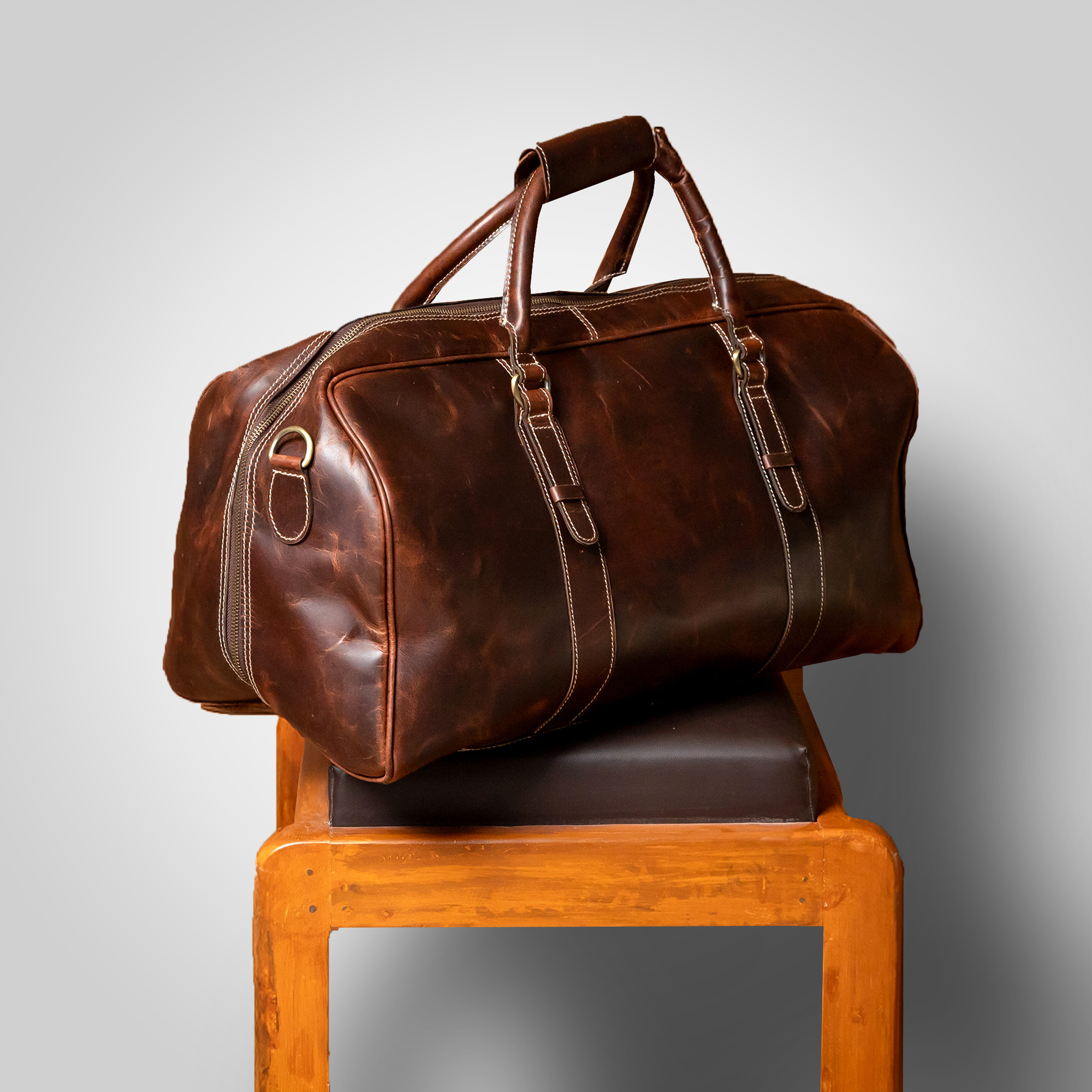 Brown leather duffel bag on a wooden chair with a gray background