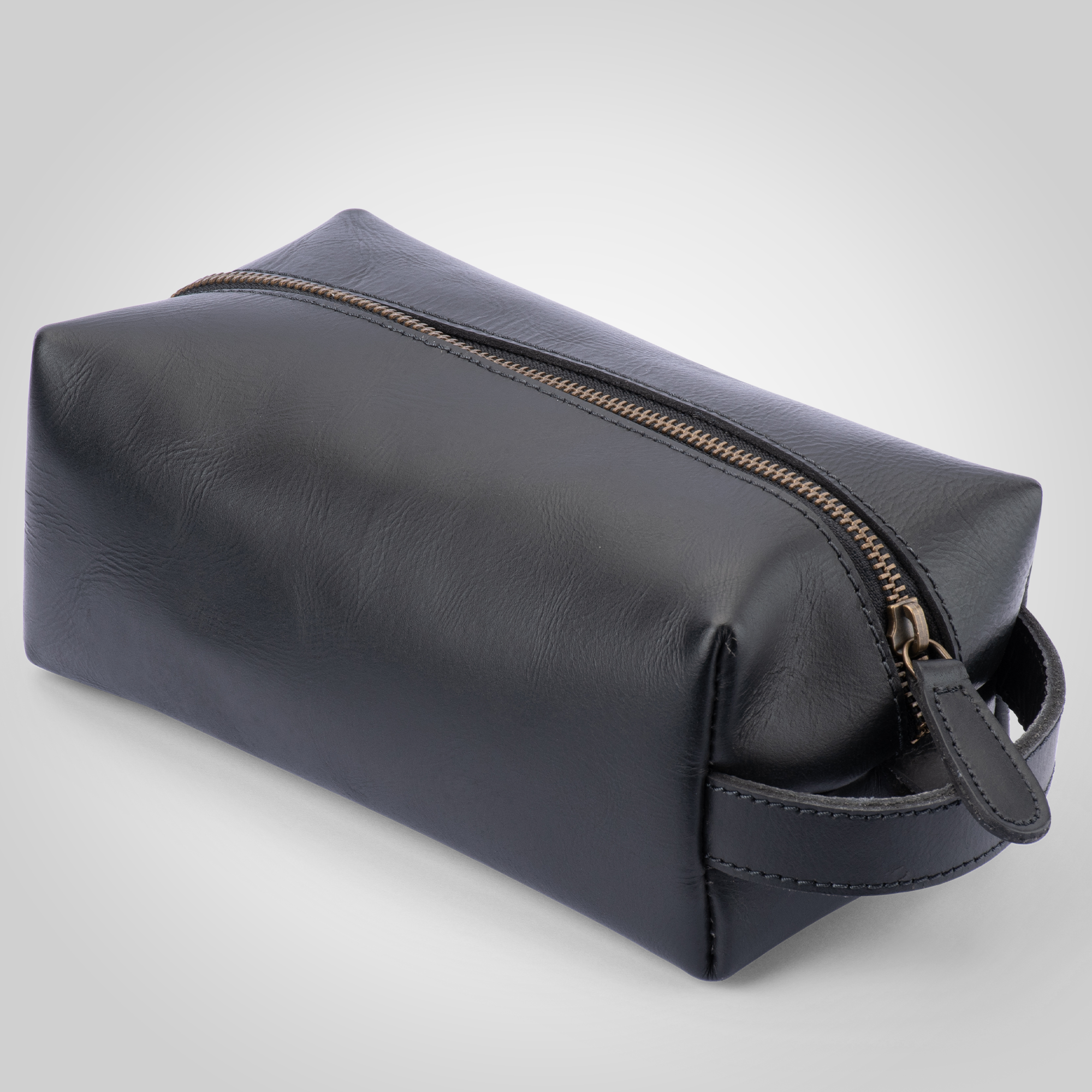 Black leather toiletry bag with gold zipper on a light gray background