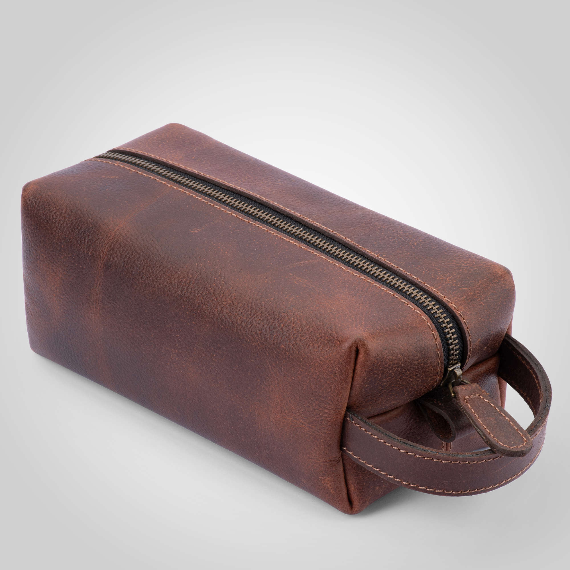 Brown leather toiletry bag with a zipper on a light gray background