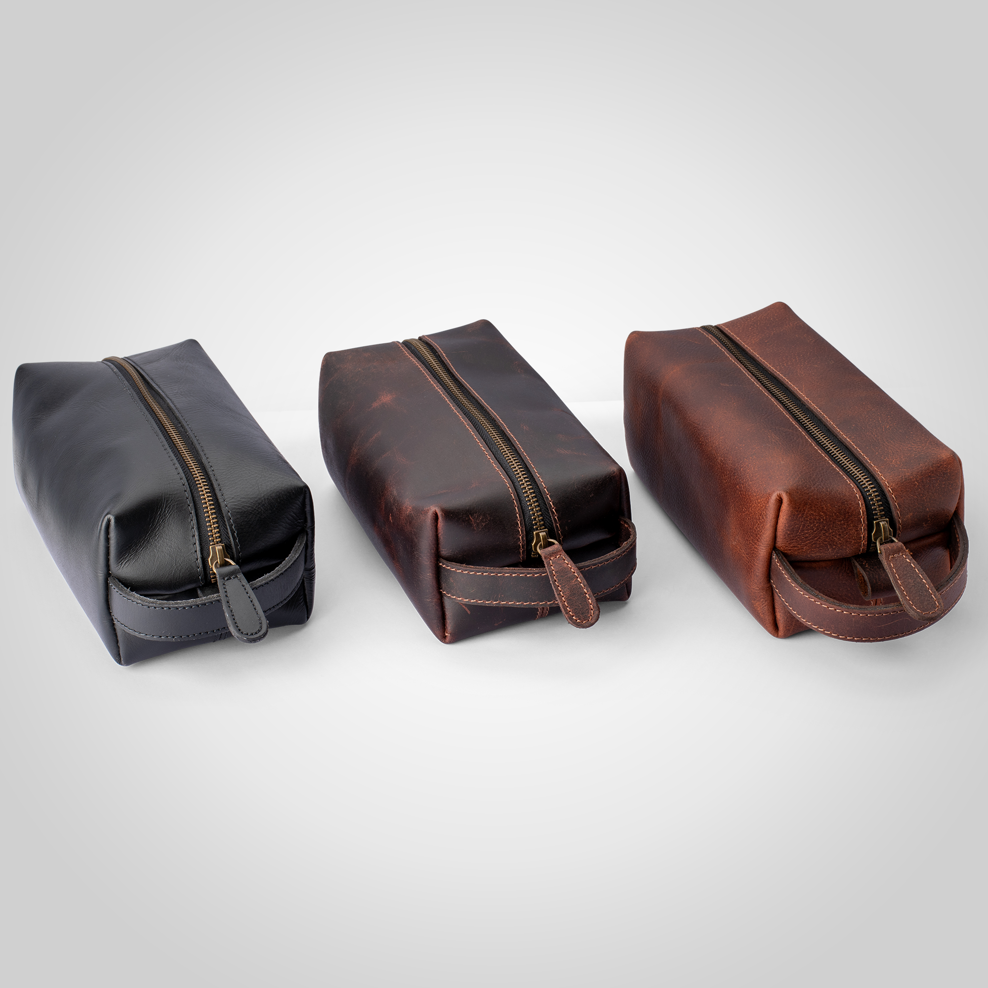 Three leather pouches with zippers in black, brown, and a reddish-brown color on a light gray background.