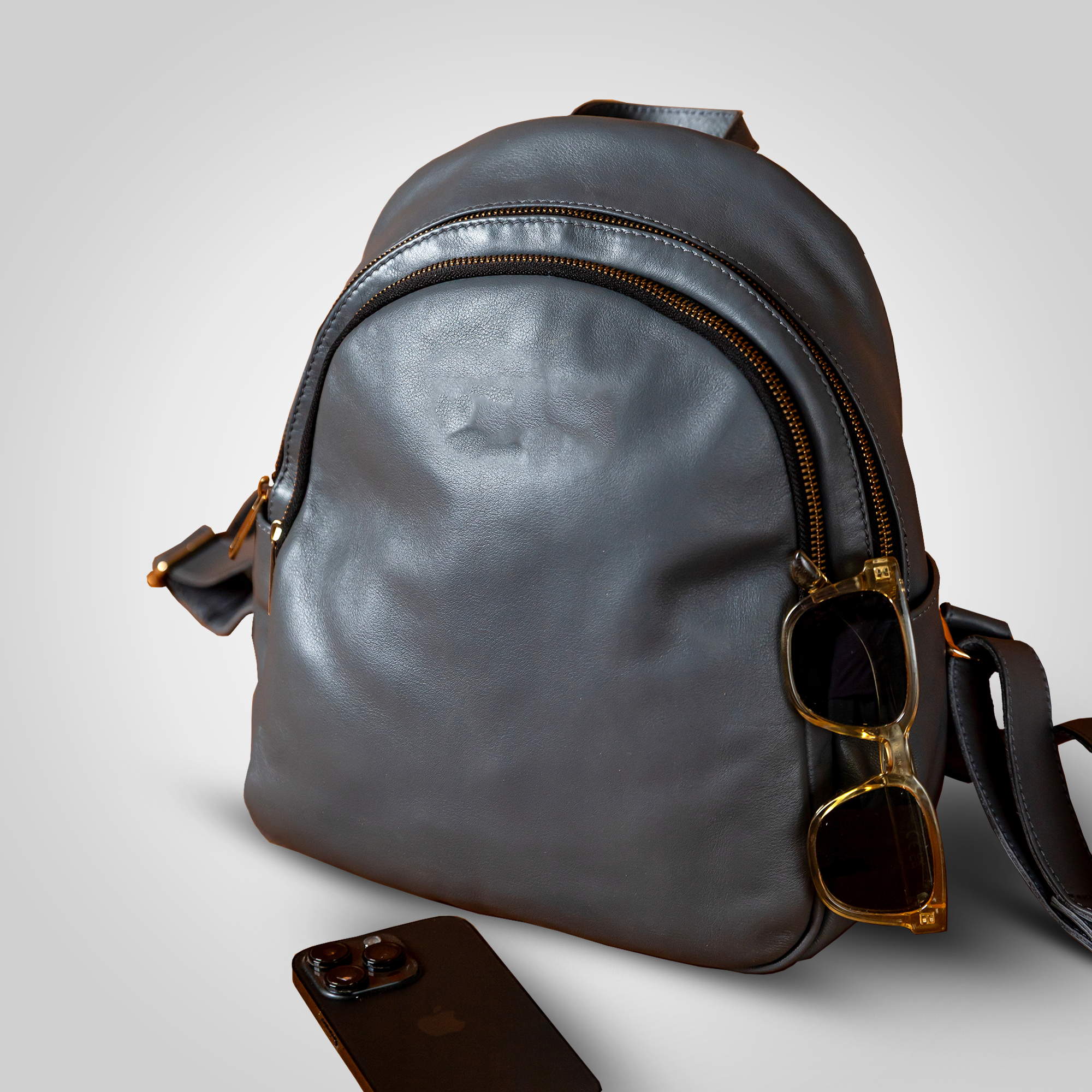 Gray leather backpack with sunglasses on a light gray background